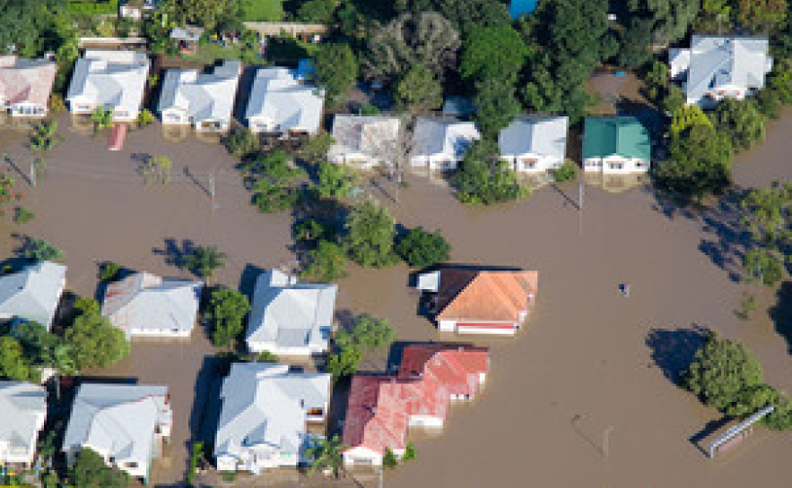 Aerial photo of a neighbourhood of houses and trees surrounding by brown flood water