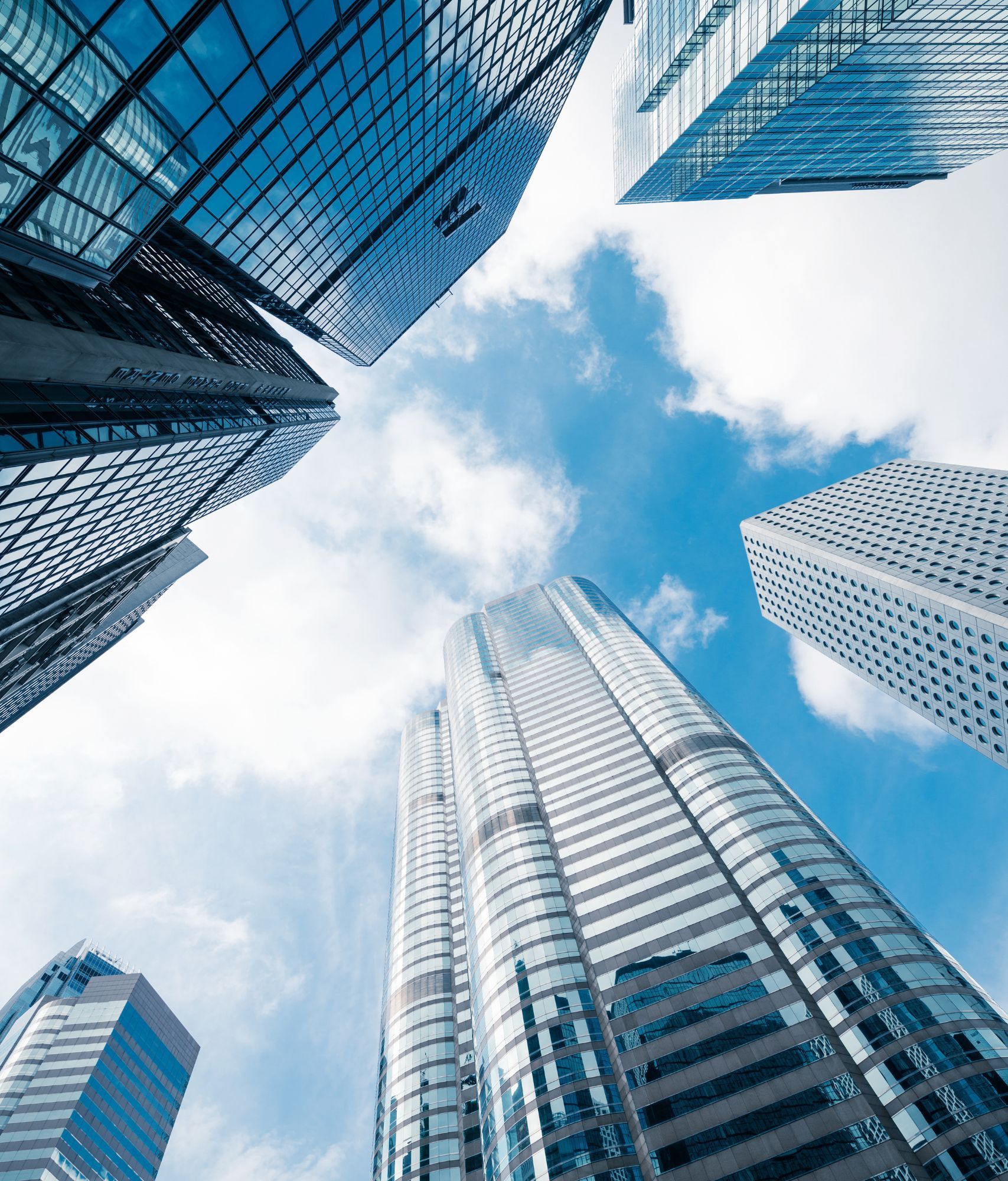 Multiple skyscrapers towering overhead against a blue cloudy sky.