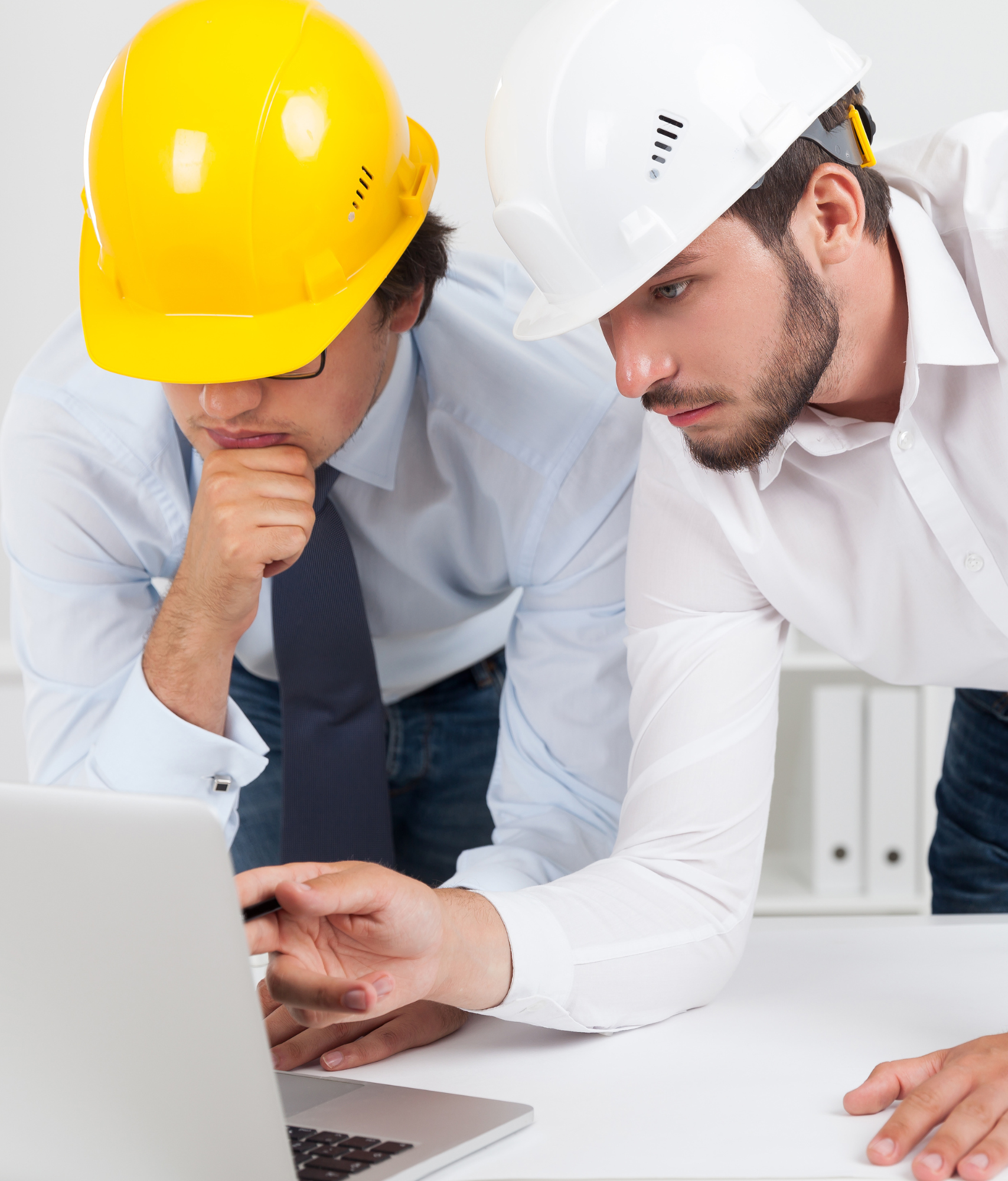 Two men in business wear and hard hats leaning over a laptop.