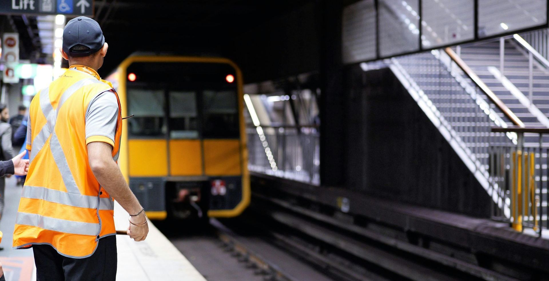 A man in an orange vest is standing on a platform next to a train.