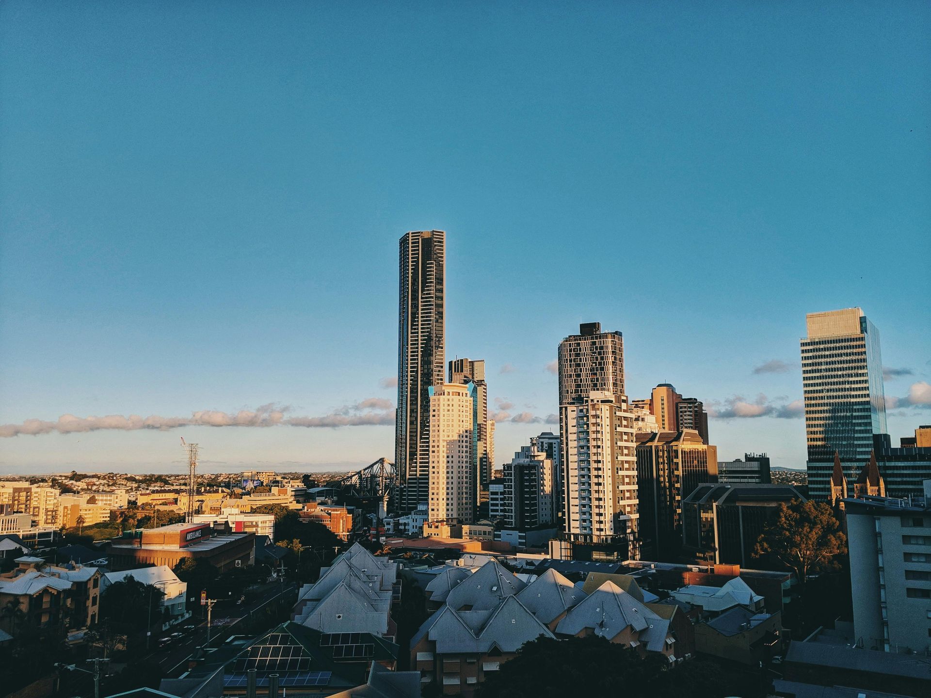 City skyline against a clear blue sky, buildings of varying heights bathed in sunlight.