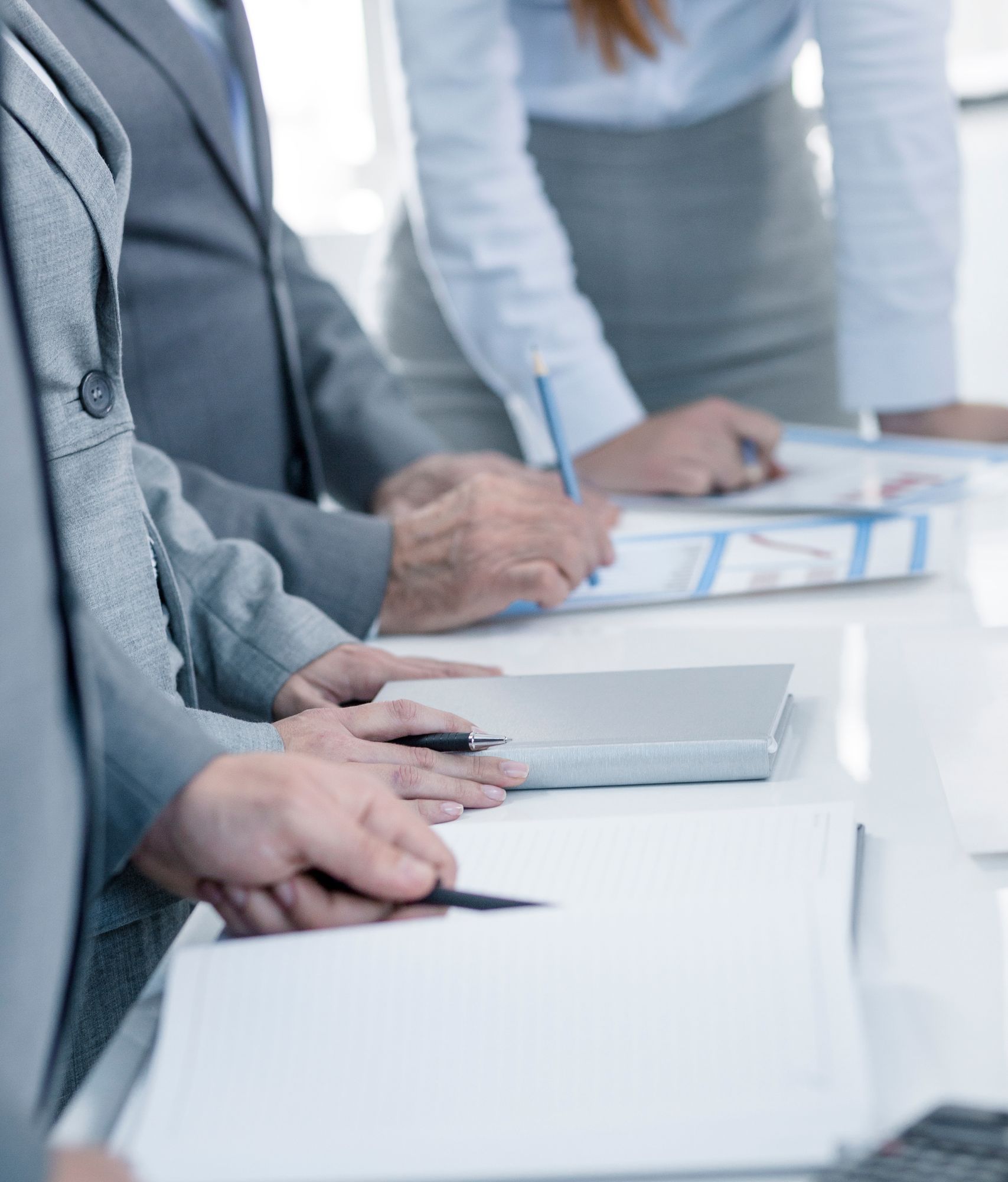 Hands of three people taking notes and examining data around a meeting table.