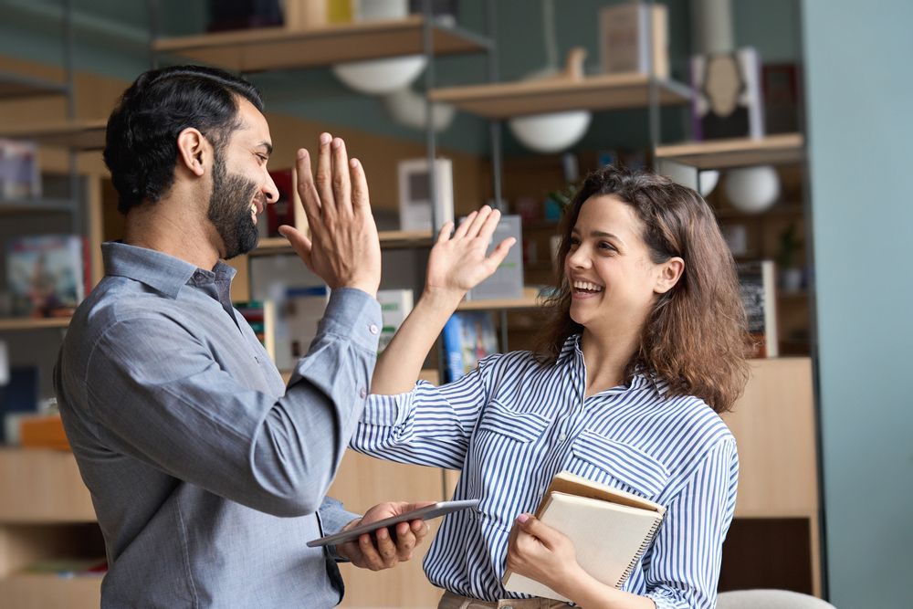 A man and a woman are giving each other a high five in an office.