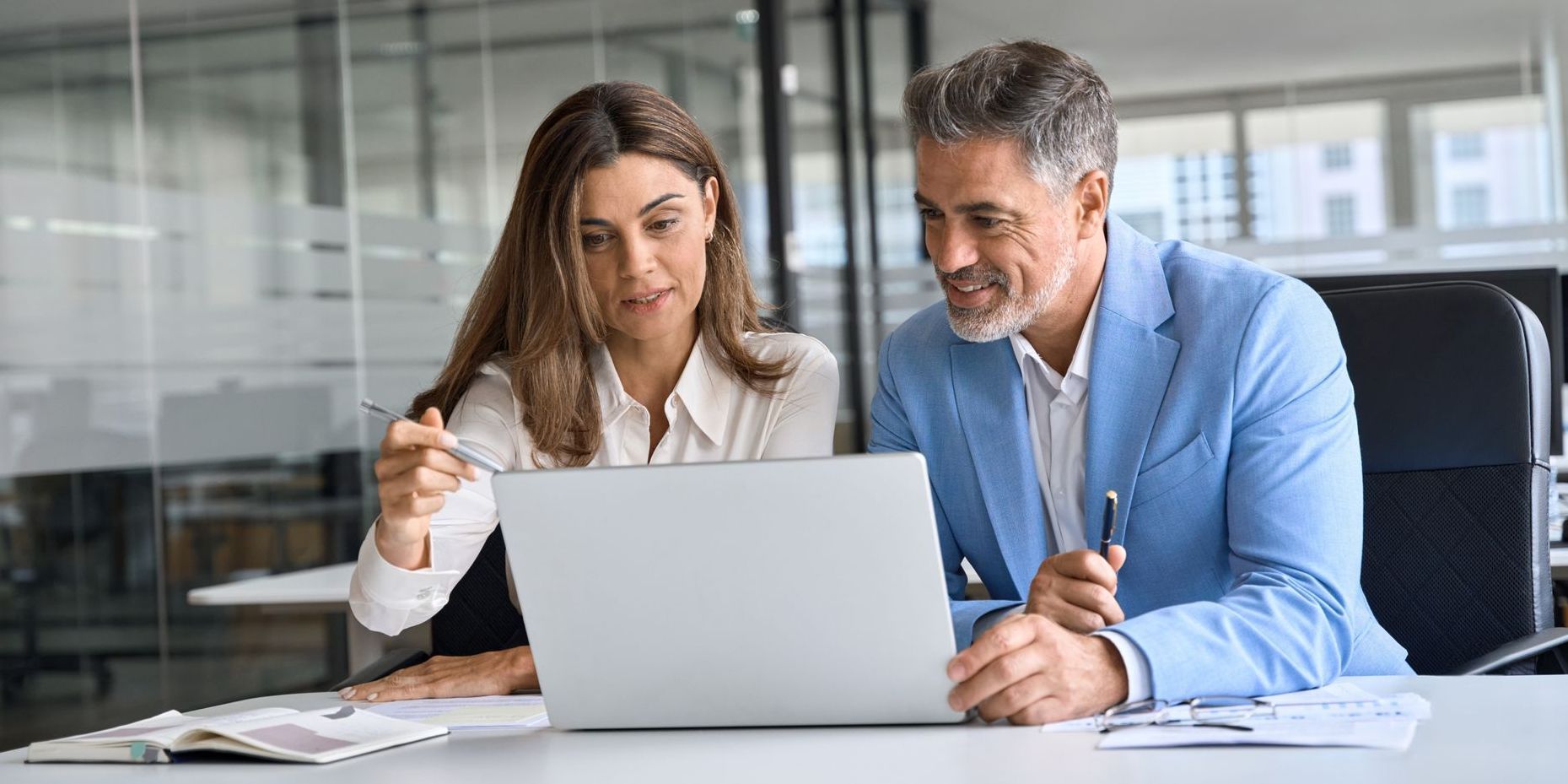 A professional man and a woman are looking at a laptop computer.