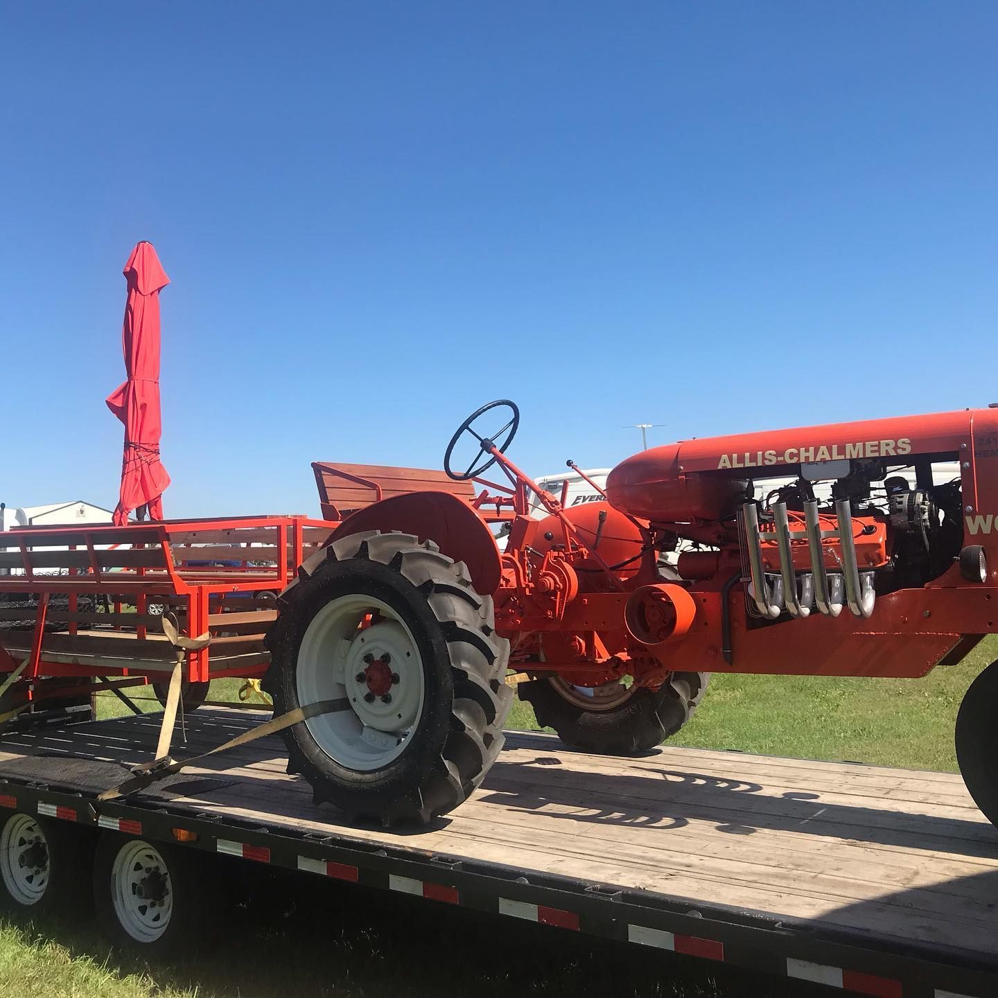 Orange Allis-Chalmers tractor pulling a red wagon on a trailer under a bright blue sky. | Don's D.I. Auto & Truck Service