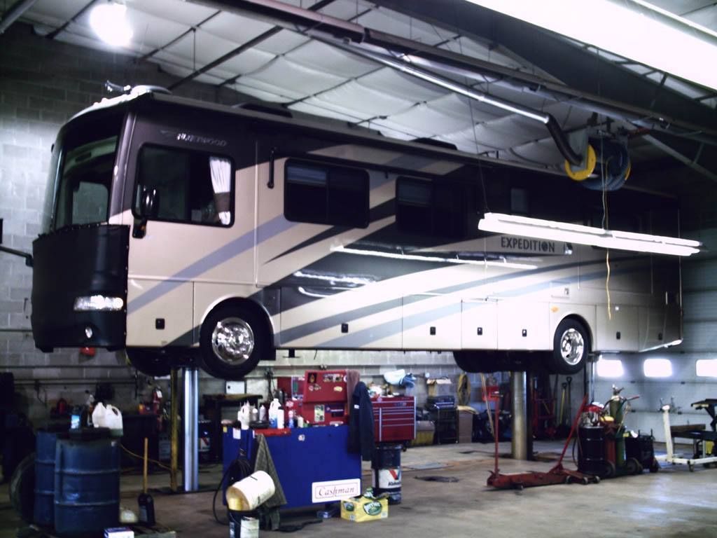 RV raised on a lift inside a repair shop. Beige and black vehicle with tools and equipment visible. | Don's D.I. Auto & Truck Service