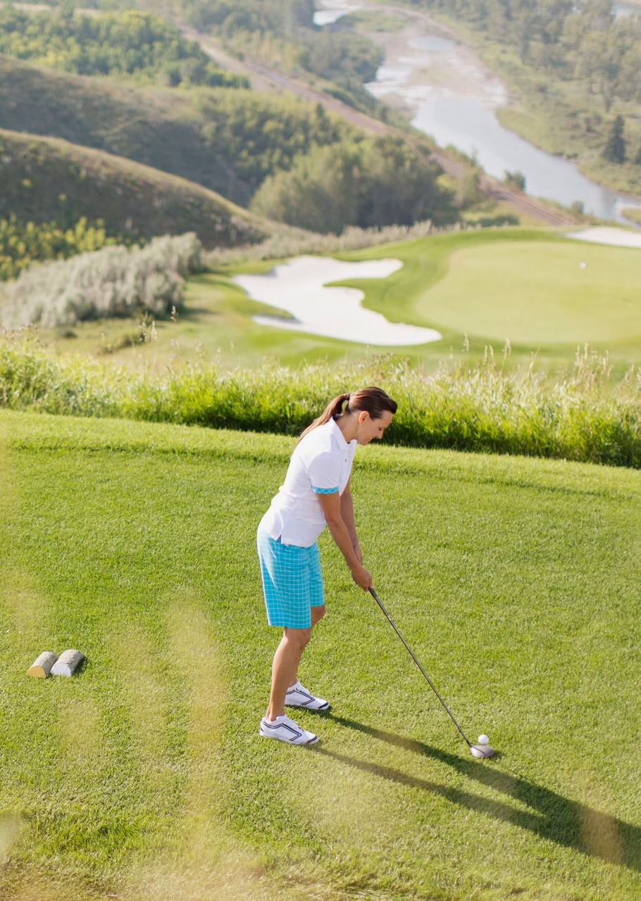 Green golf course with flag, trees, and rocks in foreground.