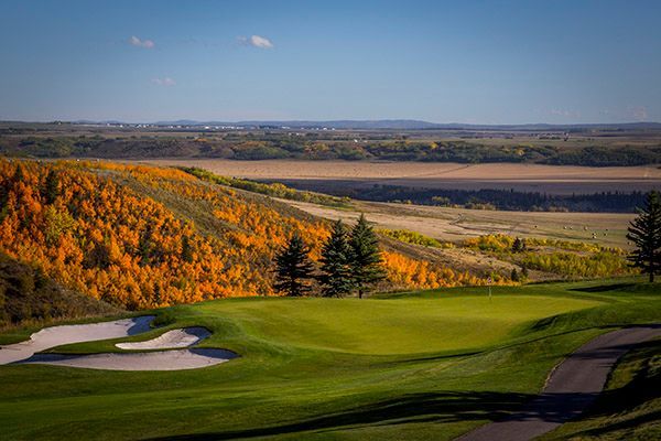 Golf course with green fairway and autumn trees, scenic landscape under blue sky.