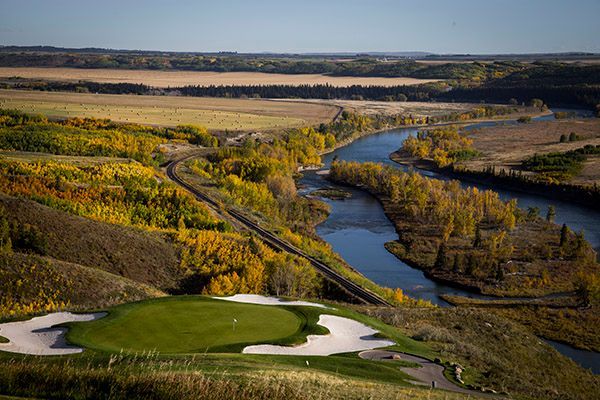 Golf course with green, sand trap, river winding through autumn landscape.