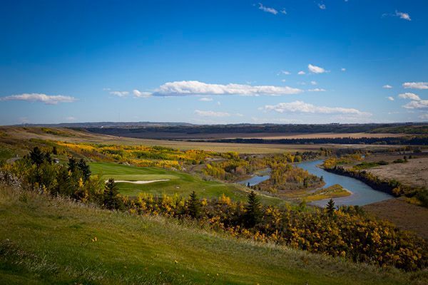 Scenic golf course with river winding through autumnal landscape under a bright blue sky.