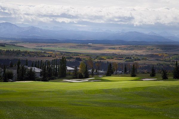 Green golf course with distant mountains under a cloudy sky.