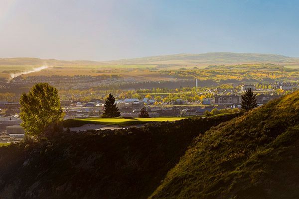 Green golf course on a hill overlooking a city during the day.