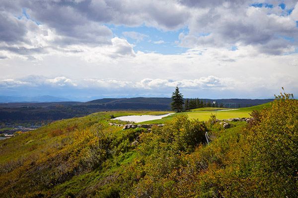 Green golf course overlooking a distant valley under a cloudy sky.