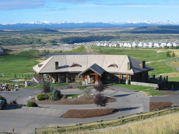 A wooden lodge with a mountain backdrop, a golf course and a driveway.