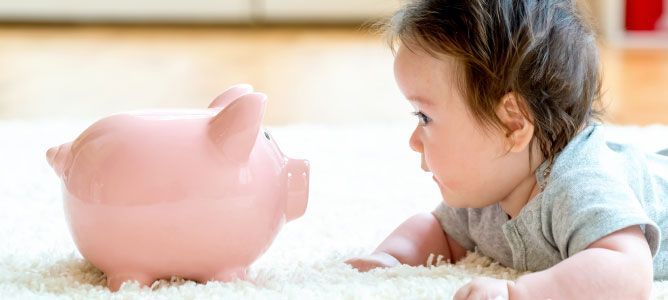 A baby is laying on the floor looking at a piggy bank.