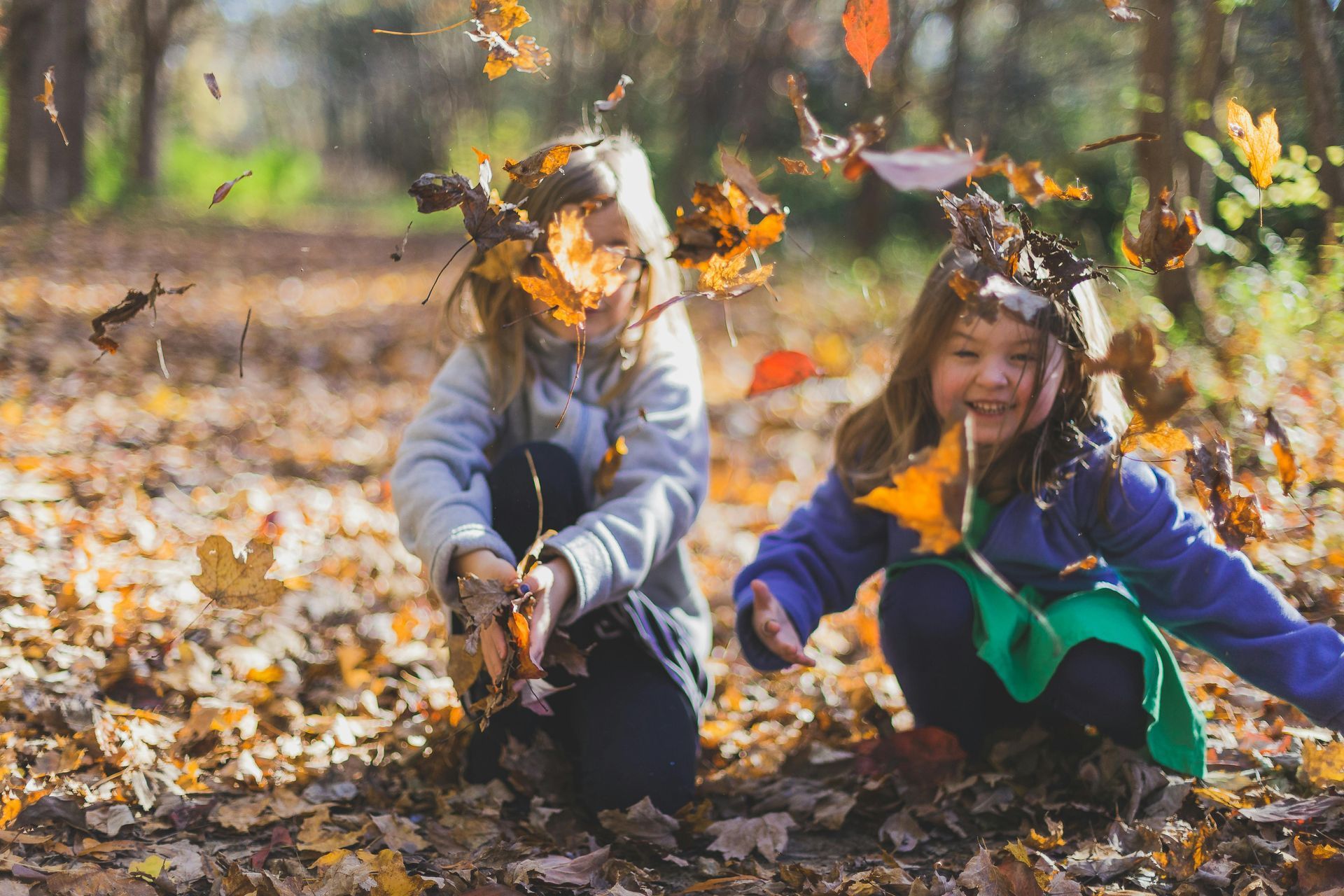 Two little girls are playing with leaves in the woods.