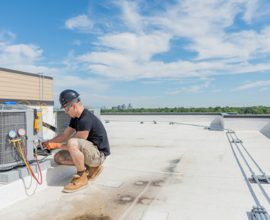 a man is kneeling on a roof working on an air conditioner .