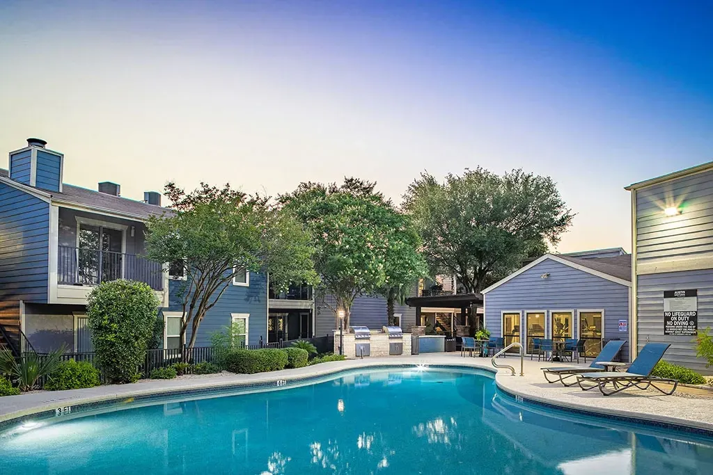 Outdoor swimming pool with lounge chairs and grilling area at apartment complex.