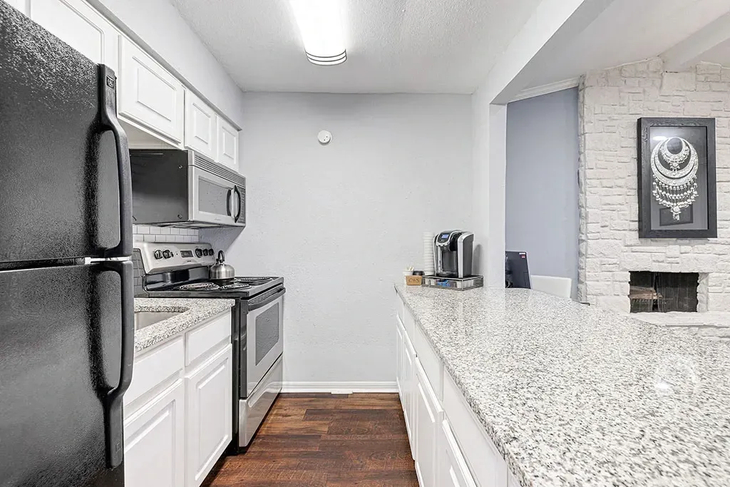 Kitchen with black refrigerator, stainless steel stove, microwave, white cabinets, and granite countertops.