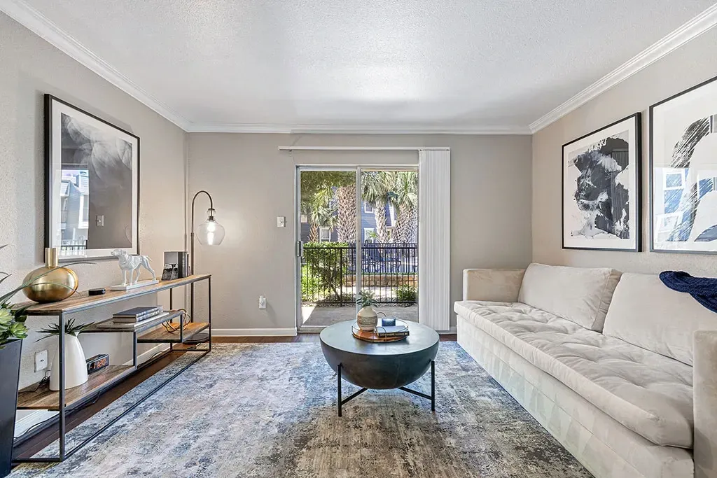 Modern living room with white sofa, coffee table, and balcony access with palm trees outside.