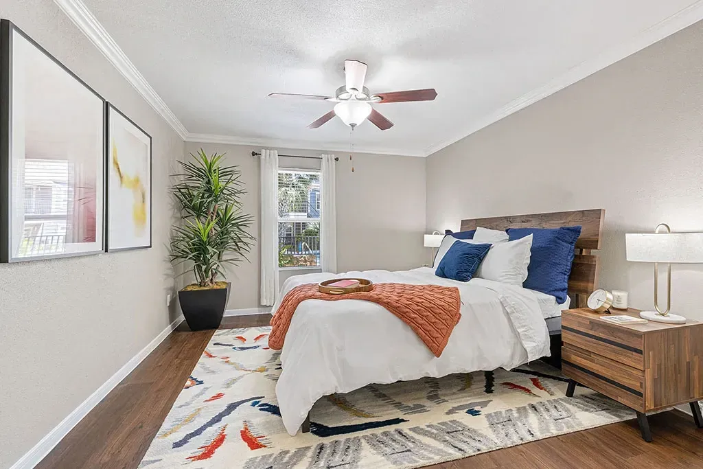 A beautifully staged bedroom with a queen-size bed, white linens, orange throw blanket, and blue accent pillows.