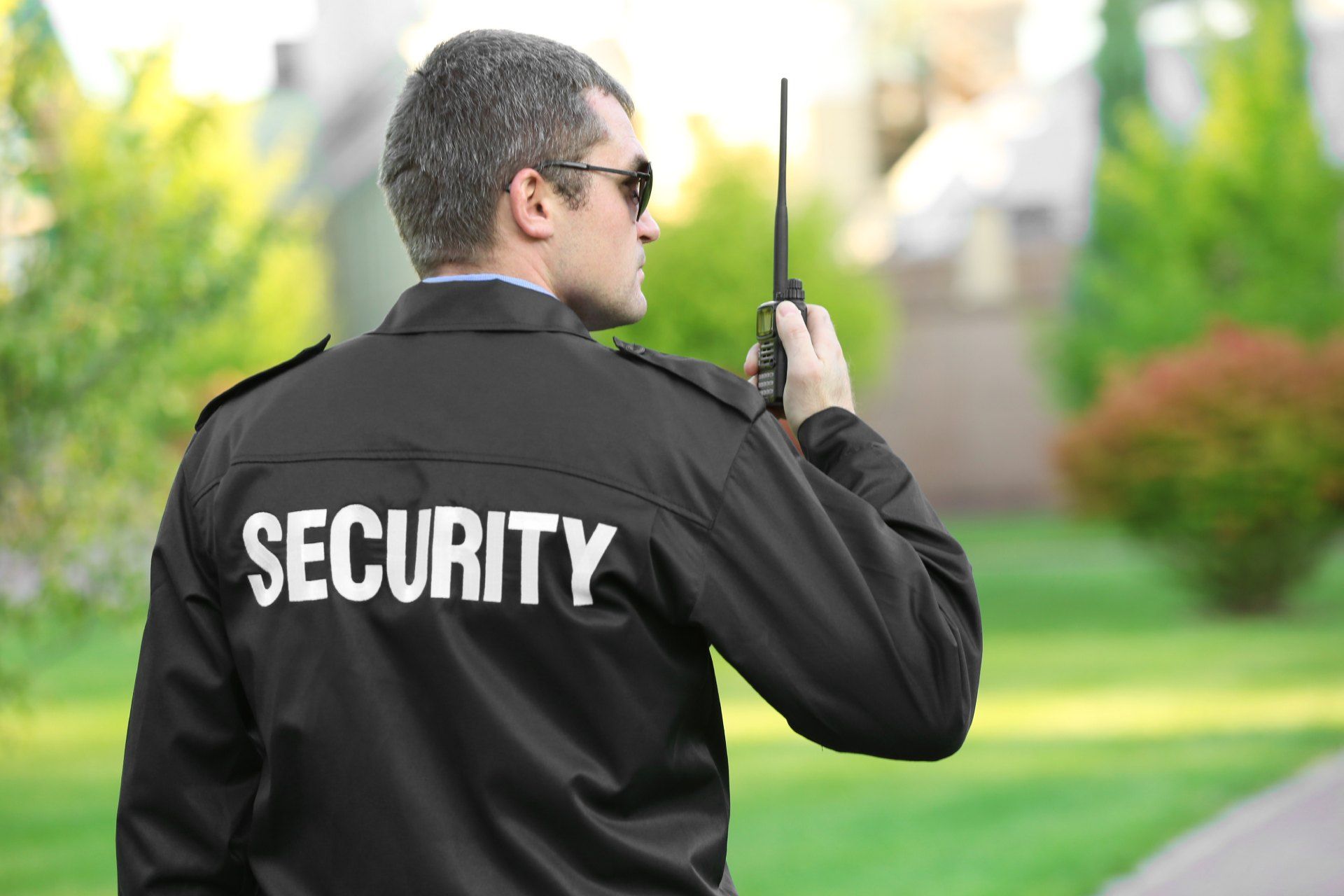 A security guard is talking on a walkie talkie in a park.