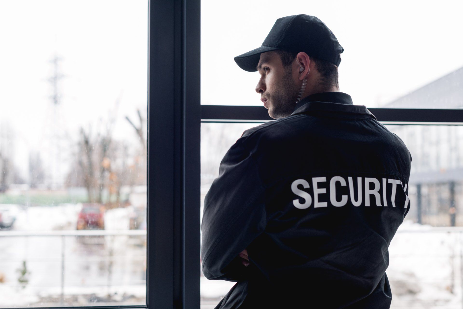 A security guard is standing in front of a window looking out.