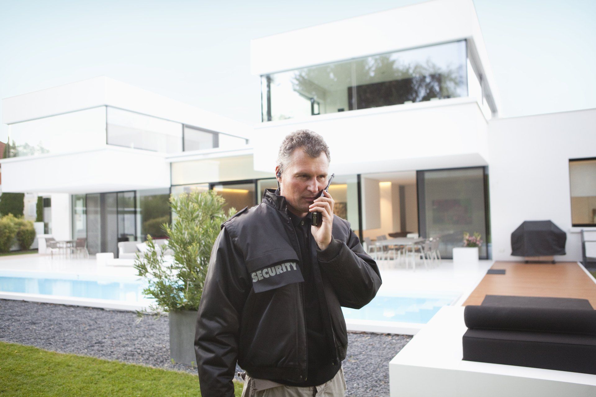 A security guard is talking on a cell phone in front of a house.