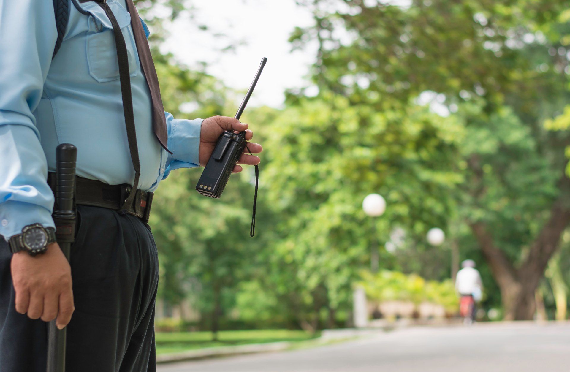 A security guard is holding a walkie talkie in a park.