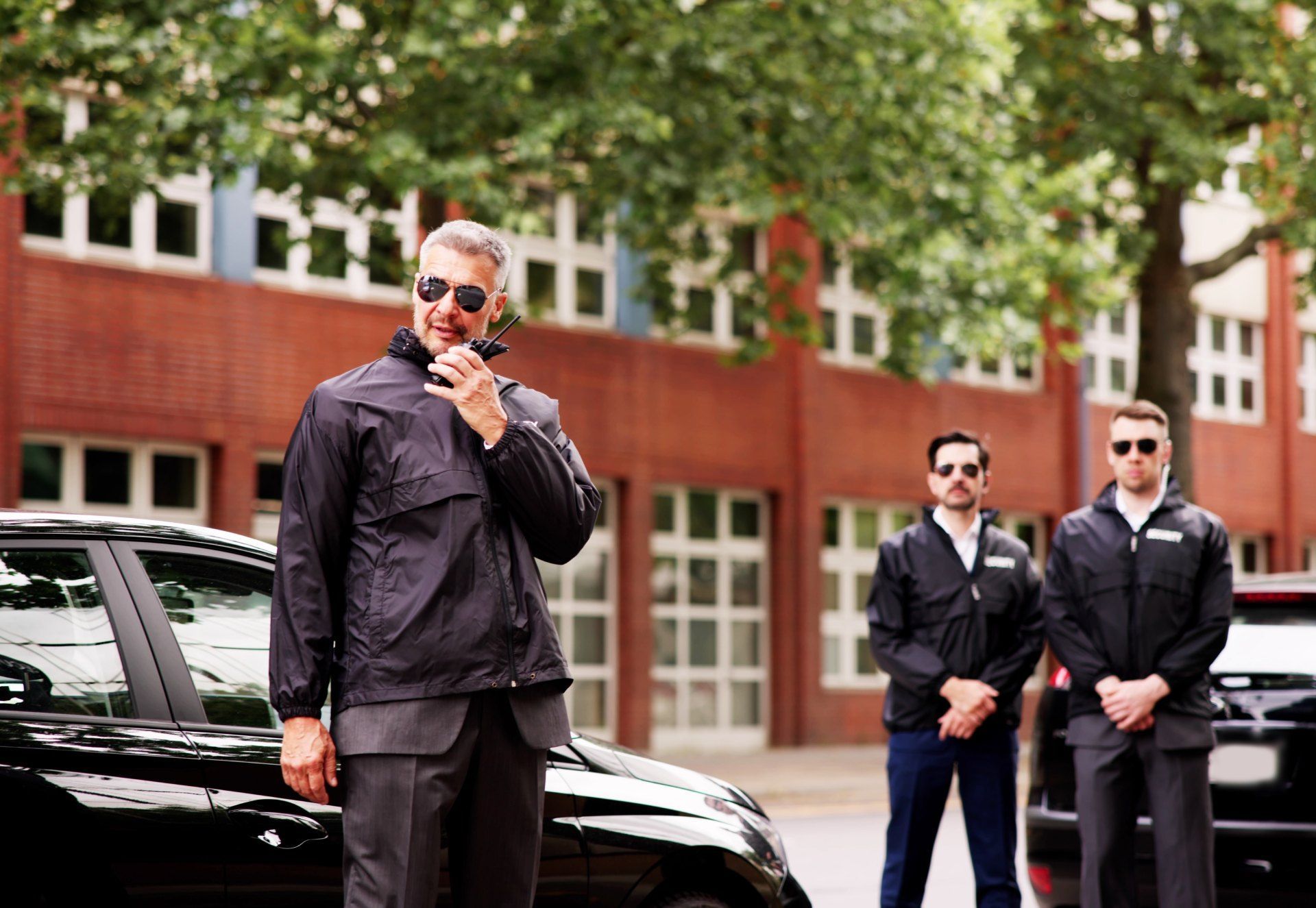A man is talking on a walkie talkie in front of a car.