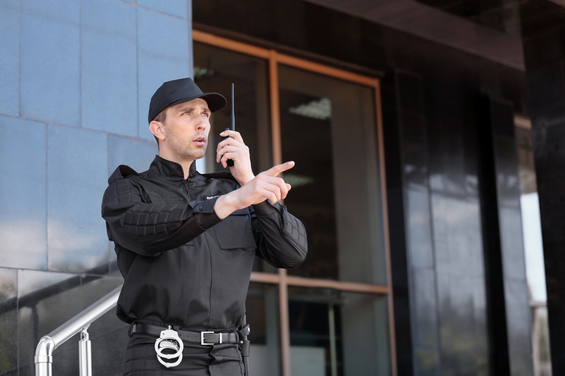A man in a black uniform is talking on a walkie talkie in front of a building.
