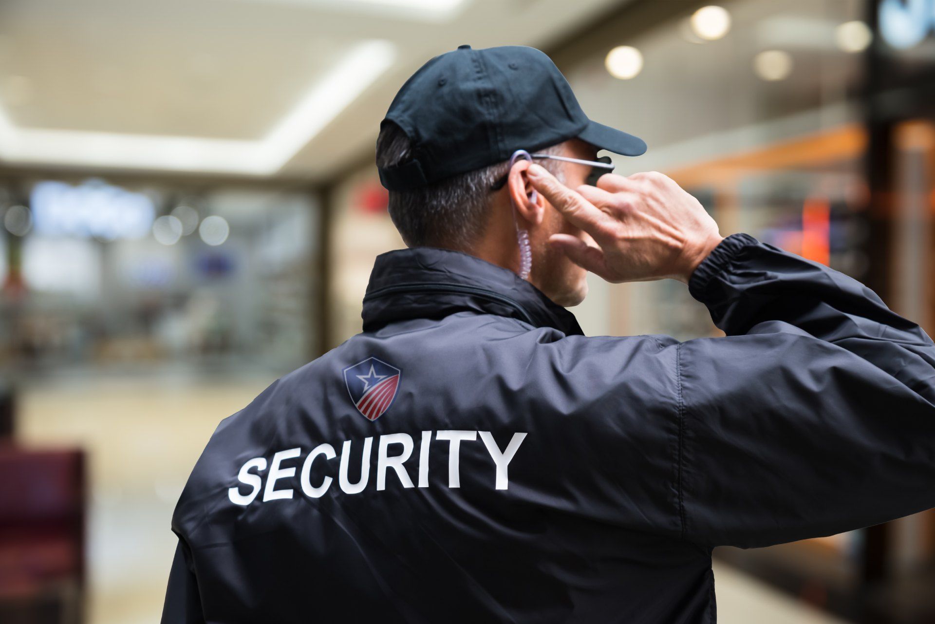 A security guard wearing a hat and sunglasses is talking on a cell phone.