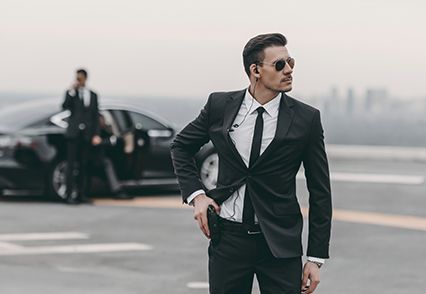 A man in a suit and tie is standing in front of a car.
