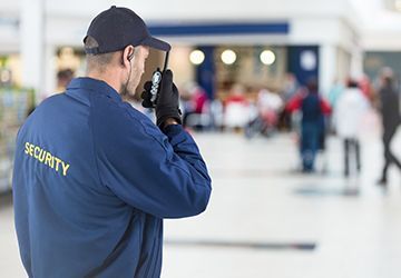 A security guard is talking on a walkie talkie in an airport.