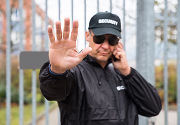 A security guard is making a stop sign while talking on a cell phone.
