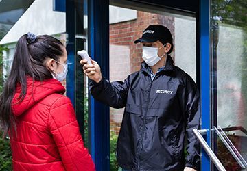 A man wearing a mask is taking a woman 's temperature with a thermometer.