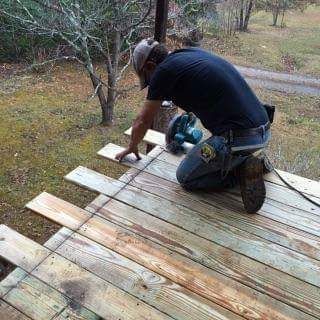 A man is kneeling down on a wooden deck using a circular saw.