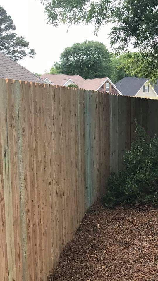 A wooden fence in a backyard with houses in the background.