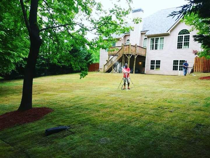 A man is mowing a lush green lawn in front of a large house