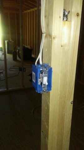 A blue box with a light switch inside of it is attached to a wooden post.