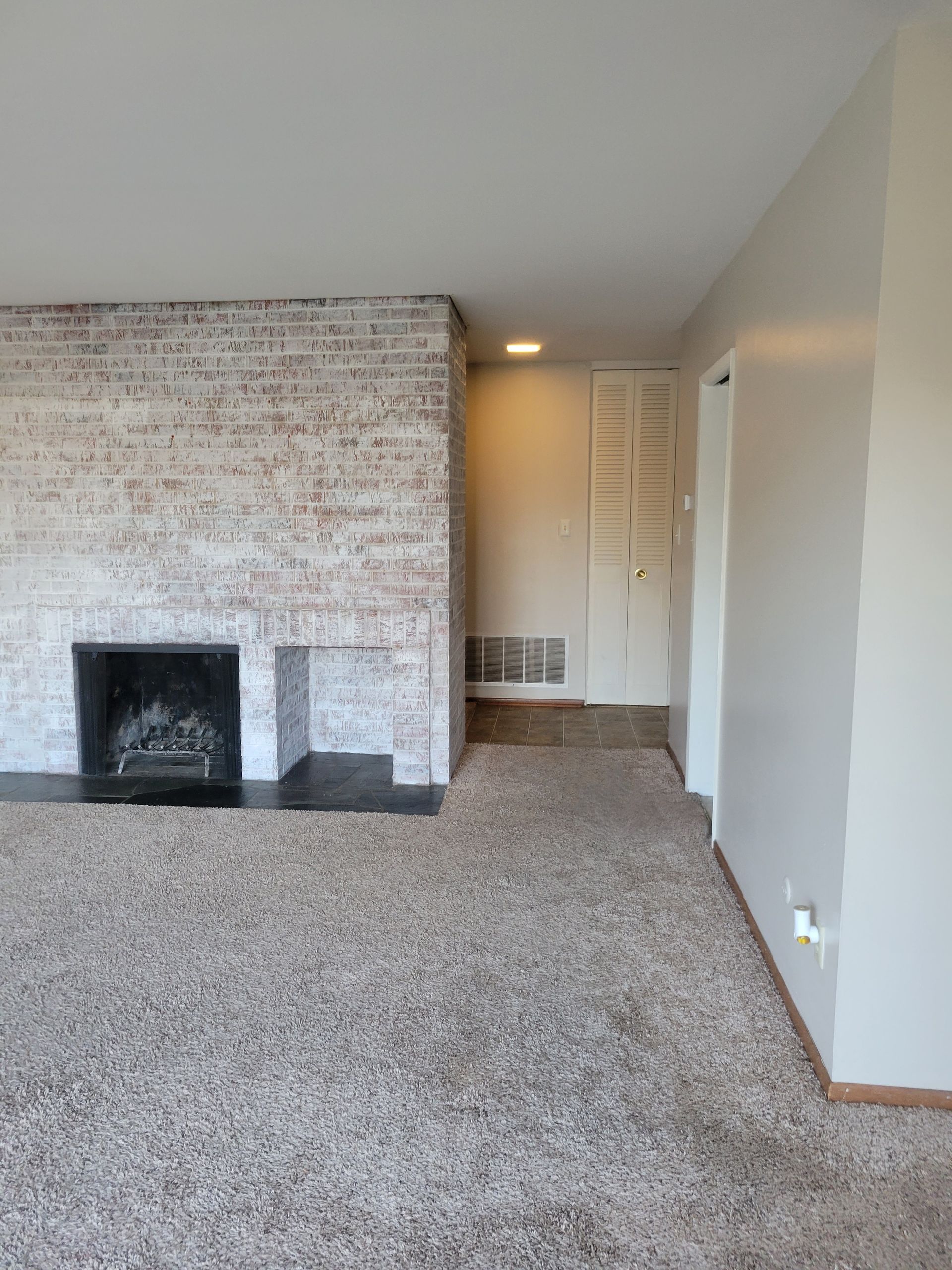 Living room with brick fireplace, light brown carpet, and white walls.