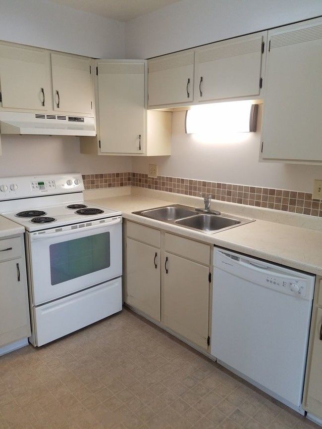 Cream-colored kitchen with stove, cabinets, sink, and dishwasher. Beige backsplash and countertops.