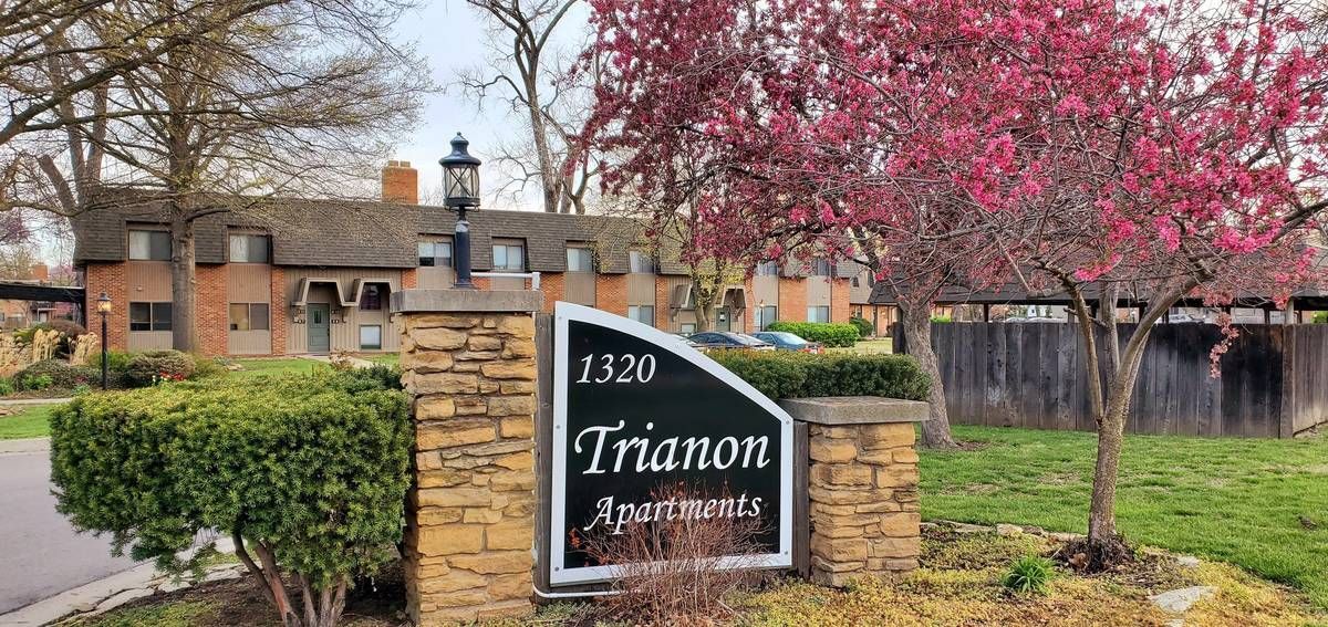 Sign for Trianon Apartments, building behind it, with red-flowered tree on the right side.
