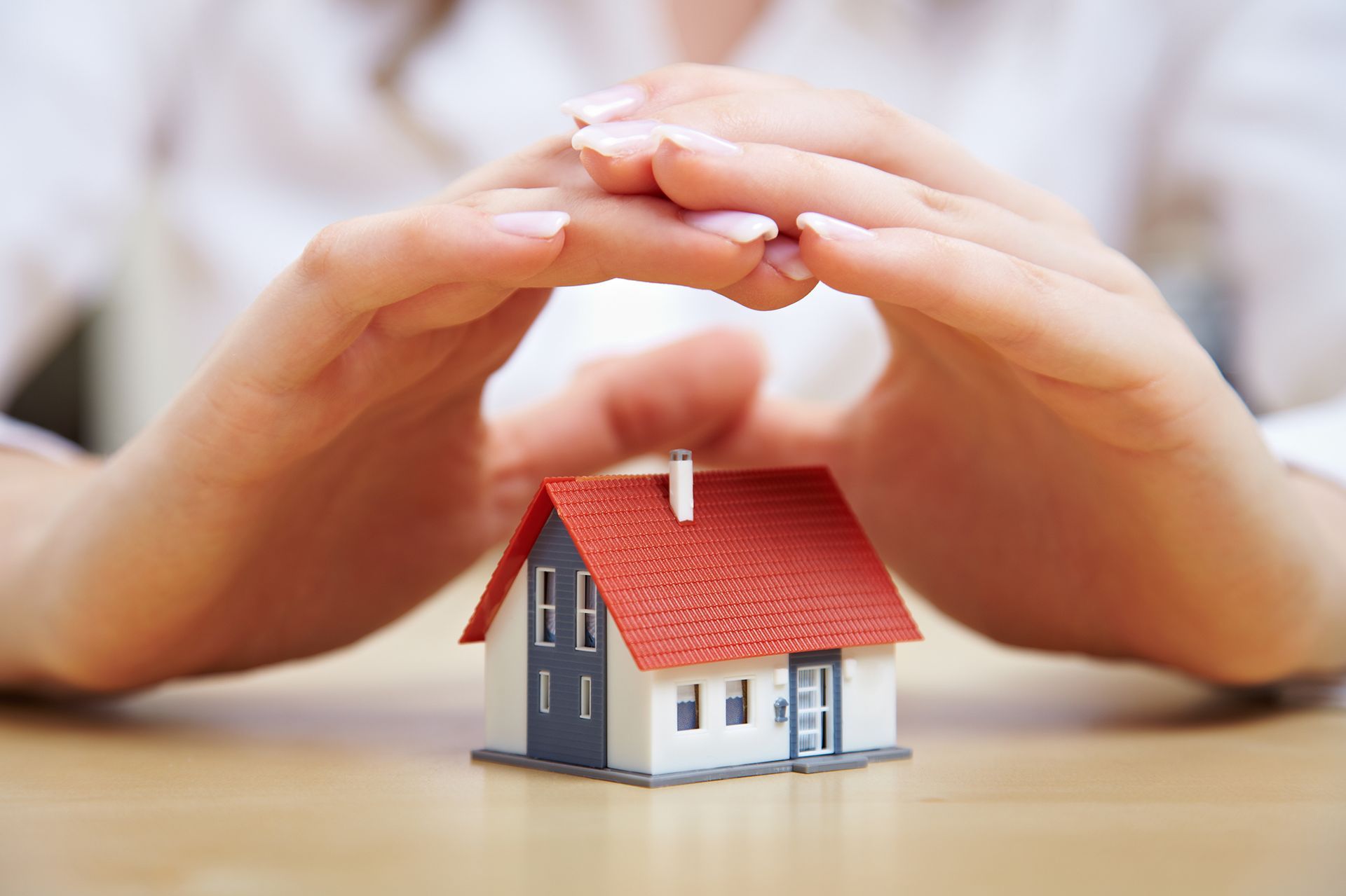 A woman is covering a small model house with her hands.