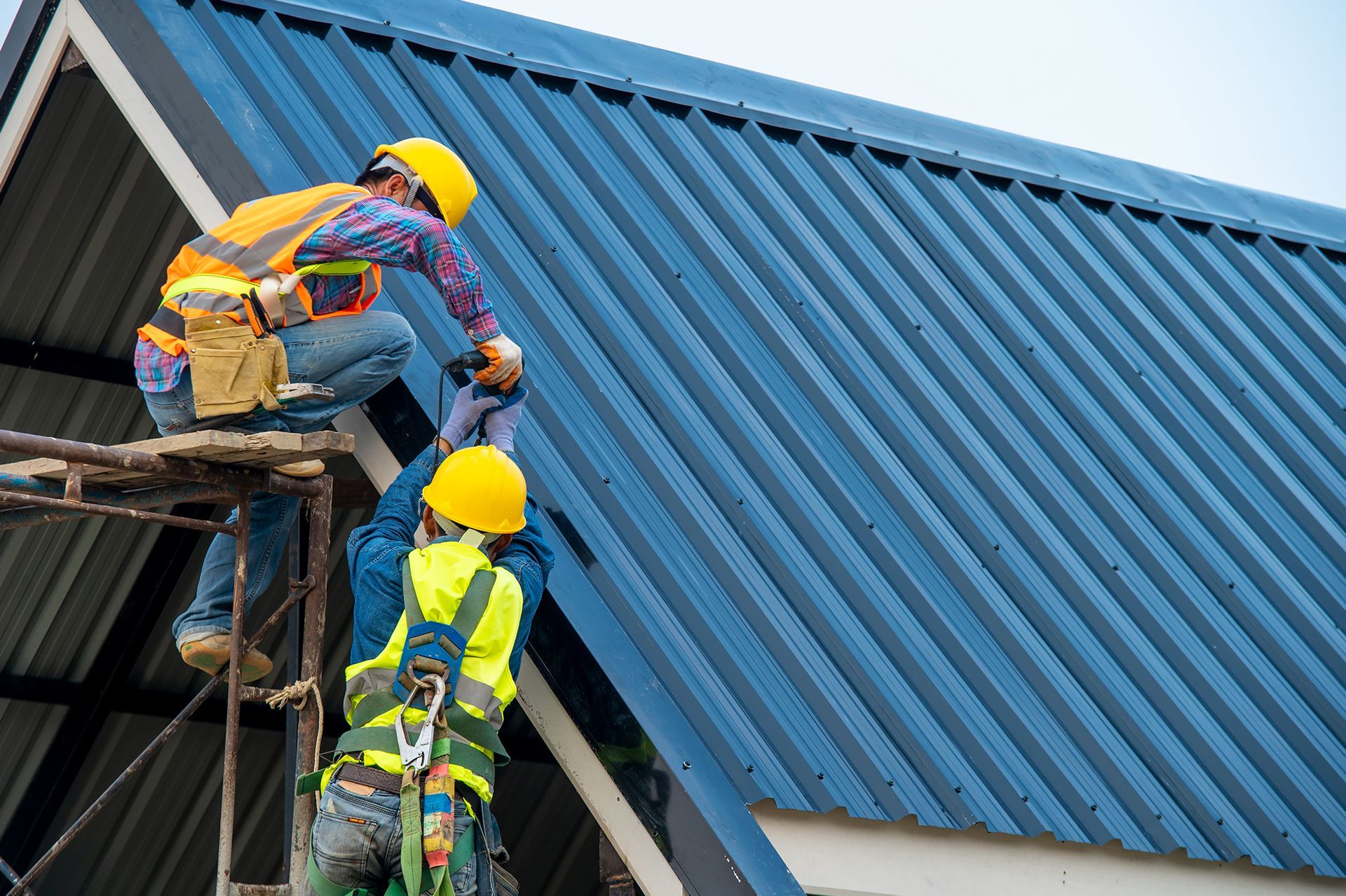 A group of construction workers are working on a blue roof.