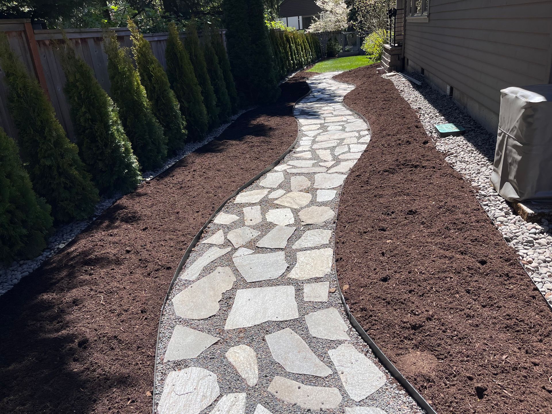 A stone walkway leading to a house in a backyard.
