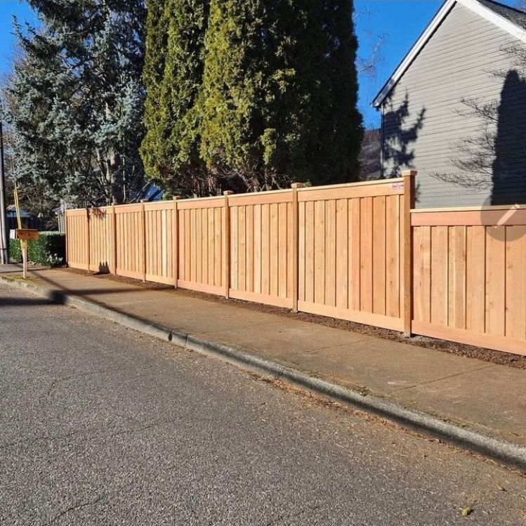 A wooden fence is along the side of a street next to a house.