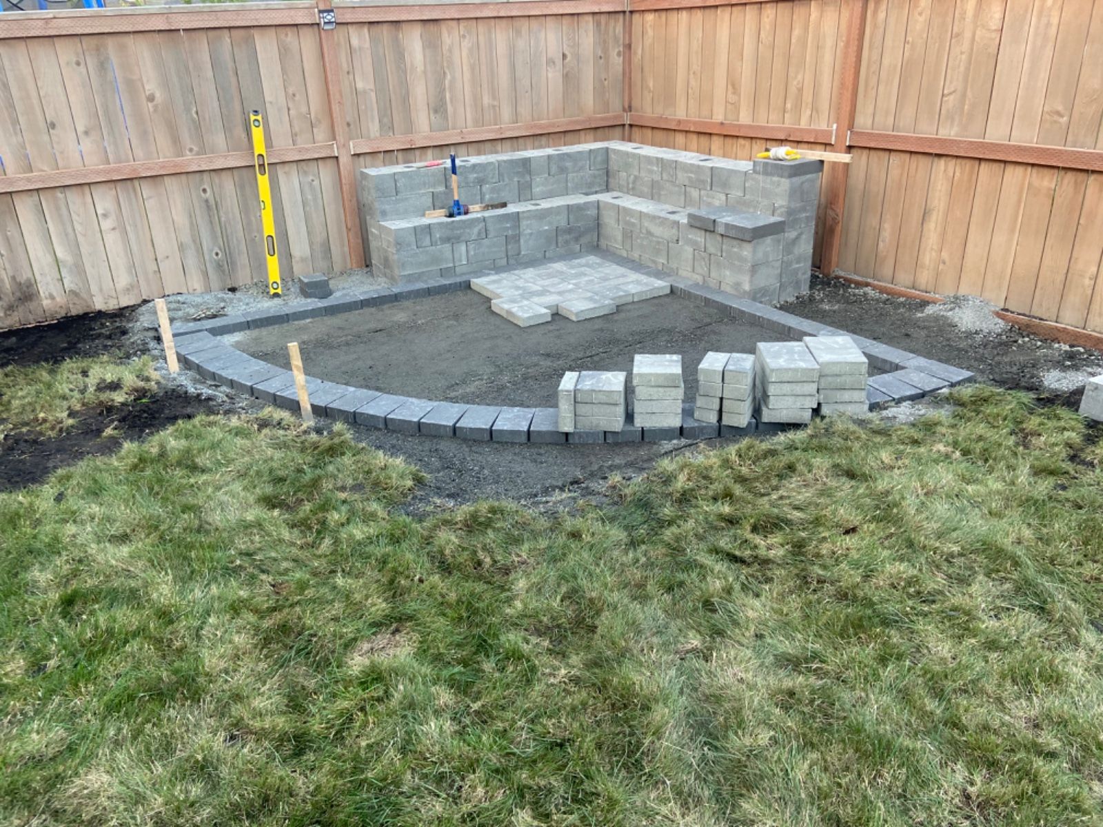 A patio is being built in a backyard next to a wooden fence.