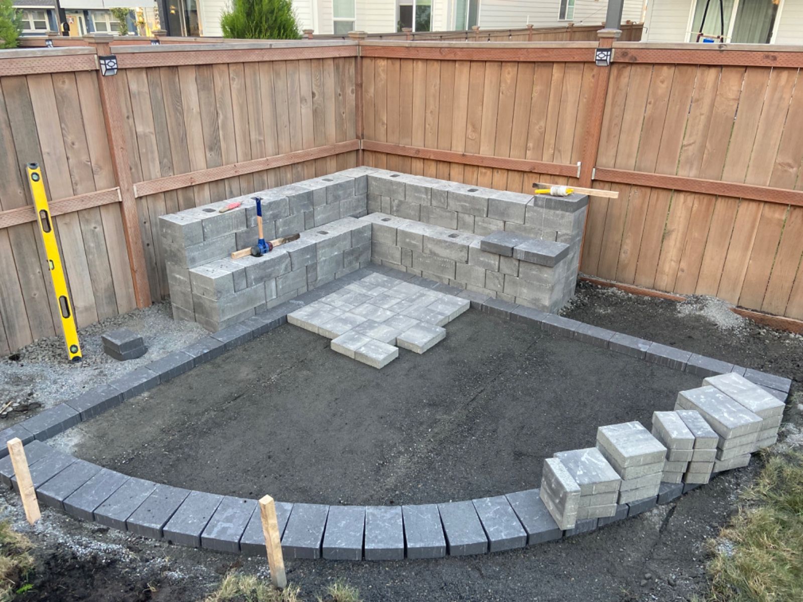 A brick patio is being built in a backyard next to a wooden fence.