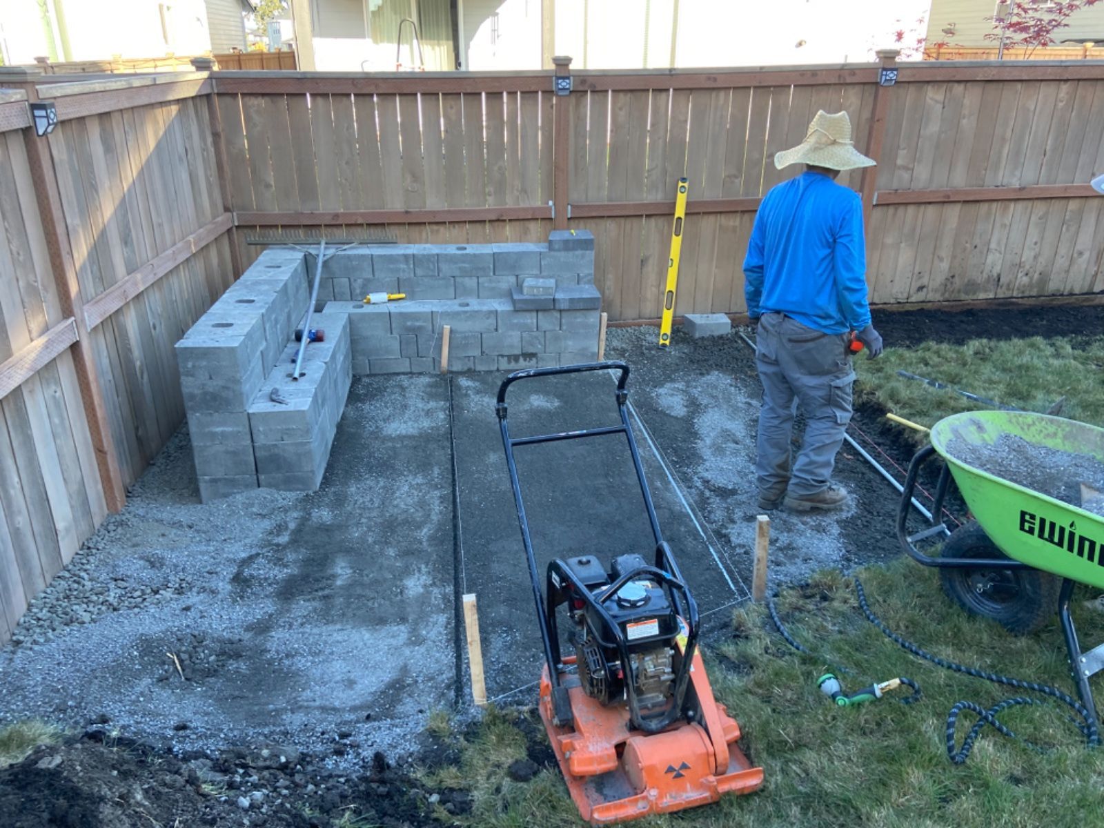 A man is standing next to a wheelbarrow in a backyard.